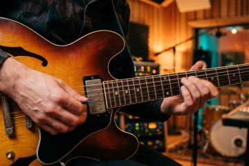 Close-up of a guitarist's hands playing a boogie shuffle on a sunburst semi-hollow electric guitar in a recording studio. 1/3