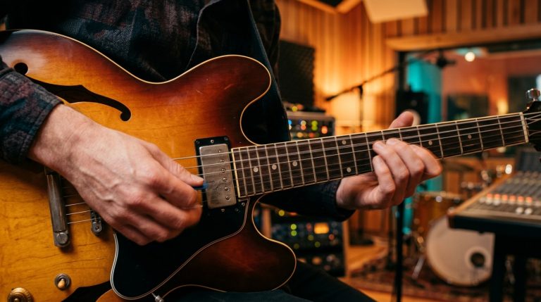 Close-up of a guitarist's hands playing a boogie shuffle on a sunburst semi-hollow electric guitar in a recording studio. 1/3