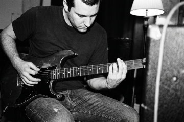 Black and white closeup of a guitarist in a small practice room practicing guitar slap picking on a boogie shuffle