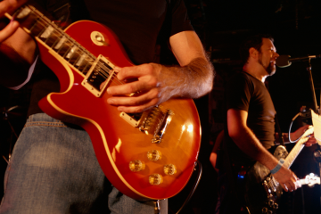 Close-up of a guitarist's red Les Paul guitar being played on stage.