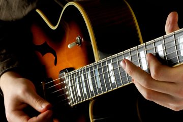 Close-up of a person playing a sunburst electric guitar, left hand on the fretboard and right hand near the strings.