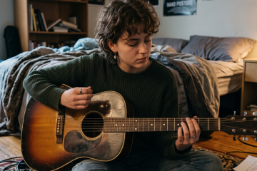 Young girl improvising on an acoustic guitar in a natural lit bedroom setting, sitting on the floor