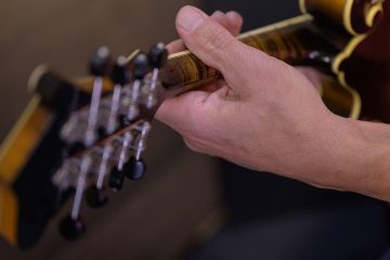 mandolin player holding the neck of a mandolin, seen from the back of the head stock