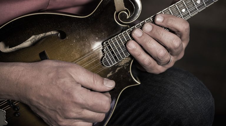 close up muted light photo of mike marshall's hands playing a Loar mandolin
