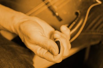 cepia tone closeup of a hand holding a blue chip mandolin pick