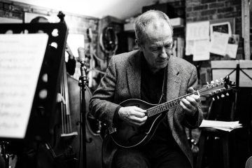 black and white photo of a man in his 50s playing mandolin in a jazz trio in a rehearsal studio