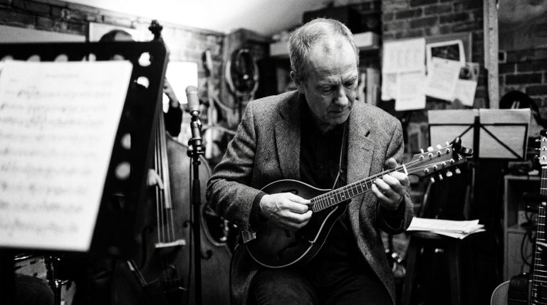 black and white photo of a man in his 50s playing mandolin in a jazz trio in a rehearsal studio