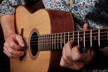 Close-up of a flatpick striking the strings of an acoustic dreadnought guitar