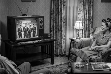 Couple watches a doo wop band perform on television in a 50's living room setting