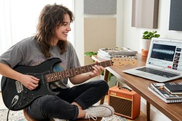 girl sits cross legged at her laptop playing a black strat and improvising over a backing track
