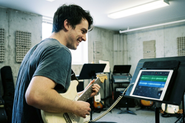 Young man practicing electric guitar improvising on a single string using an ipad to play a track