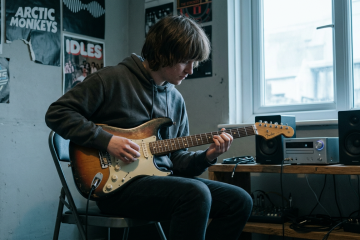 young boy with electric guitar practices in his bedroom playing improv along with his favorite song