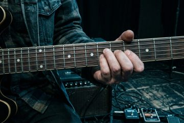 close up photo of fretting hand playing single-note muted figures on a dimly lit stage