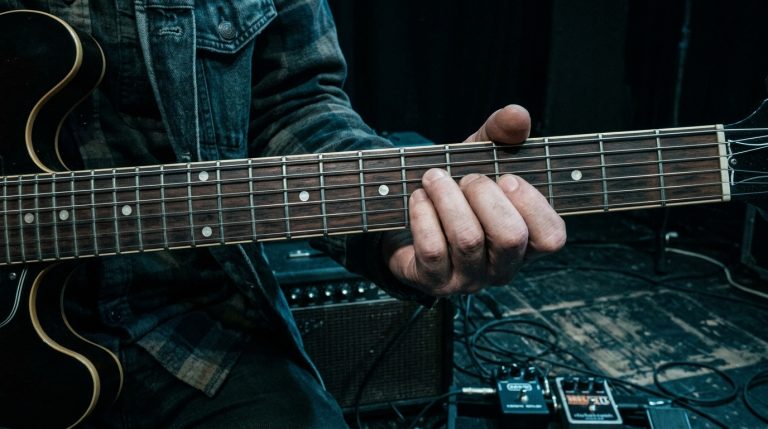 close up photo of fretting hand playing single-note muted figures on a dimly lit stage