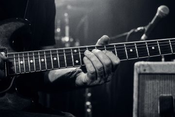 a close up black and white photo of a guitarist soloing on a smoky stage with amps in the background for a big guitar tone