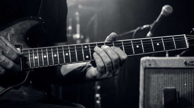 a close up black and white photo of a guitarist soloing on a smoky stage with amps in the background for a big guitar tone