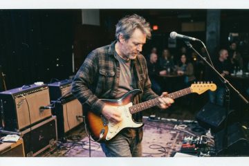 a blues guitar player plays an improvised lead on a small stage thumb muting for an intentional sound