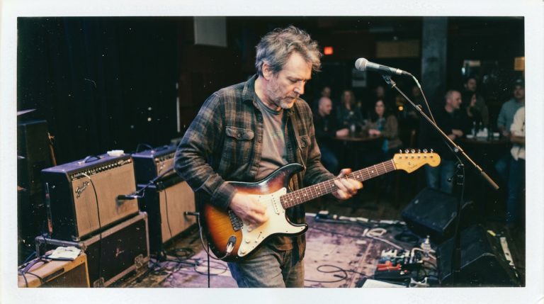 a blues guitar player plays an improvised lead on a small stage thumb muting for an intentional sound