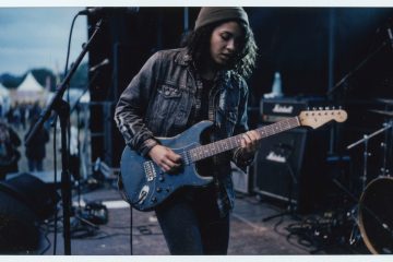 a young female guitar player solos on an outdoor stage demonstrating triplet fills over a blues shuffle groove
