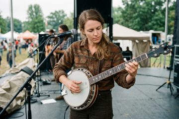 a women in her 20's plays banjo backup while a guitarist takes a solo at a bluegrass outdoor festival