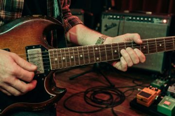 guitar player practices 16th notes on an SG style guitar in a low lit practice room.