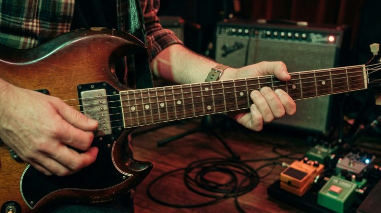 guitar player practices 16th notes on an SG style guitar in a low lit practice room.