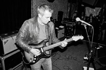black and white photo of a middle aged man playing live over the V chord in a 12 bar blues jam