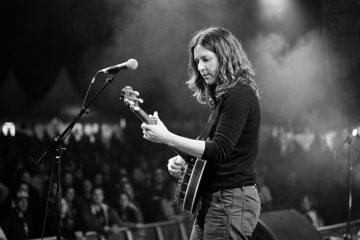 black and white photo of a female banjo player playing banjo backup on stage at a night