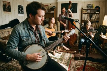 a young bluegrass band practices a jam in a living room, the banjo player demonstrates backup over a mandolin solo