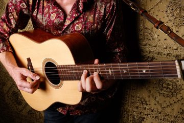 Tyler Grant close up photo in a studio with Tyler playing a flatpicking guitar break