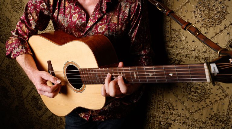 Tyler Grant close up photo in a studio with Tyler playing a flatpicking guitar break
