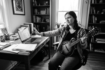 a woman rejects her laptop as she plays mandolin in her home office, skeptical of the technology after asking musicians about AI