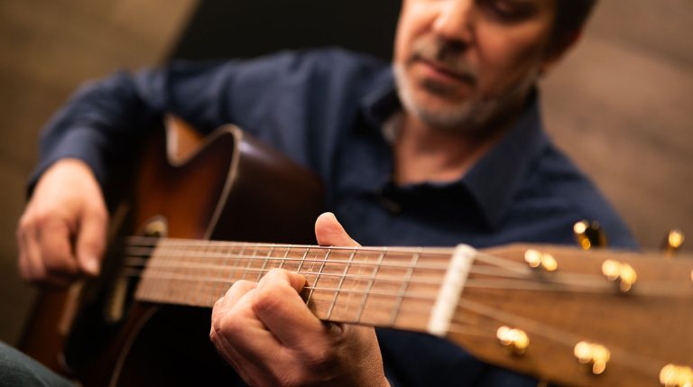 Dave Isaacs in the studio playing an acoustic guitar teaching how to practice a new song