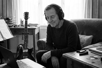 a guitar player in his 60's focused intently to listen to a song through headphones