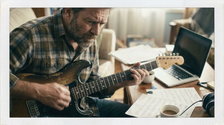 a man in his 50's practices how to use a chord chart on an electric guitar in a home practice room