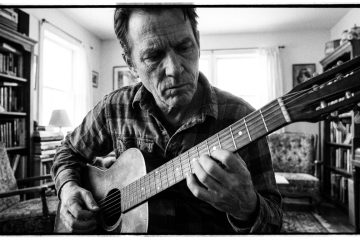 a man practices his acoustic guitar, experimenting with single notes vs. chords for textural control