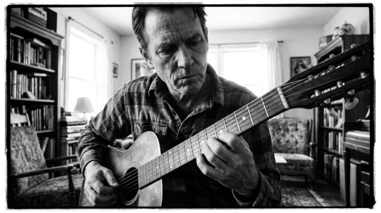 a man practices his acoustic guitar, experimenting with single notes vs. chords for textural control